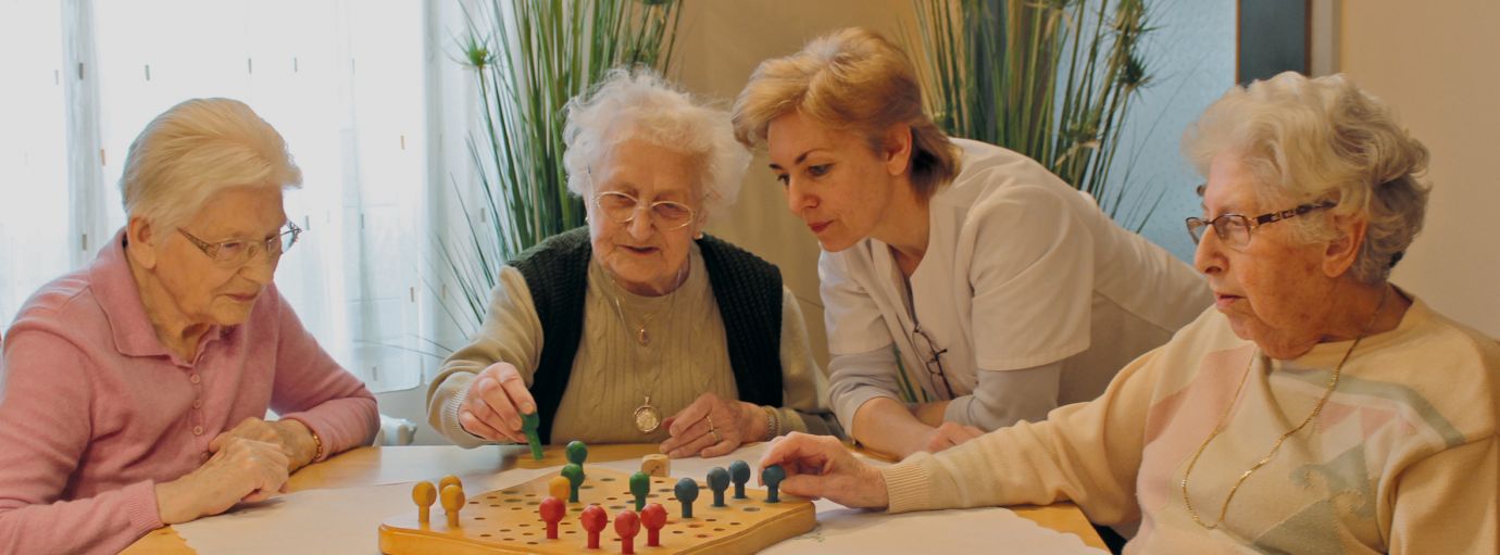 drei alte Damen und Betreuungskraft beim Brettspiel